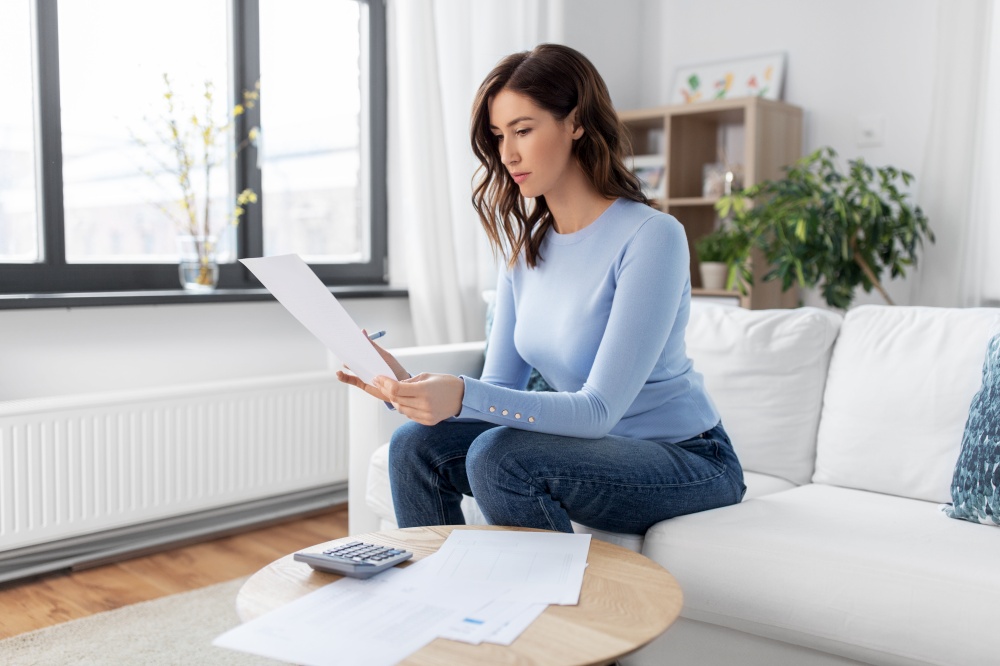 accounting, taxes and finances concept - young woman with papers and calculator at home. woman with papers and calculator at home
