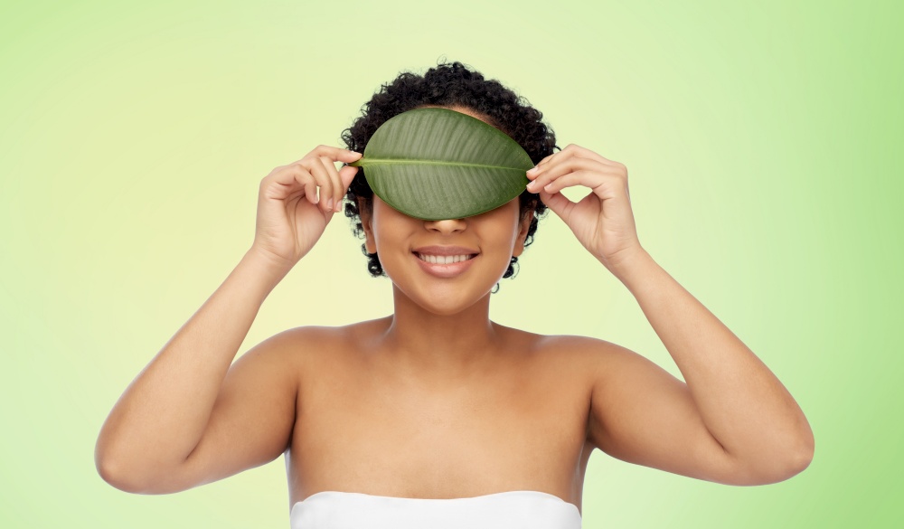 beauty, nature and people concept - portrait of happy smiling young african american woman with leaf on her face over lime green natural background. portrait of african american woman with green leaf