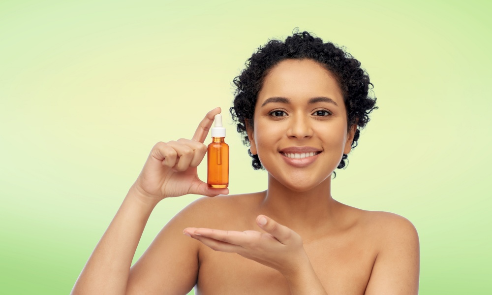 beauty, cosmetics and skincare concept - portrait of happy smiling young african american woman with bare shoulders holding bottle of serum or face oil over lime green natural background. happy african american woman with bottle of serum
