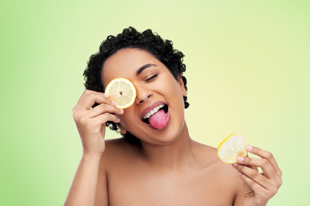 beauty, skin care and detox concept - beautiful african american woman making eye mask of lemons over lime green natural background. african american woman making eye mask of lemons