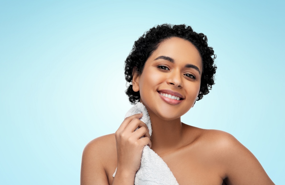 beauty and people concept - portrait of happy smiling young african american woman with bath towel over blue background. young african american woman with bath towel