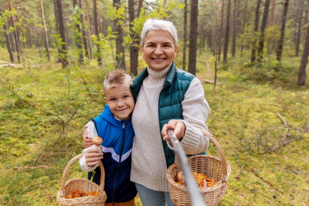 picking season, leisure and people concept - happy smiling grandmother and grandson with mushrooms in baskets taking picture with selfie stick in forest. grandmother and grandson with baskets take selfie