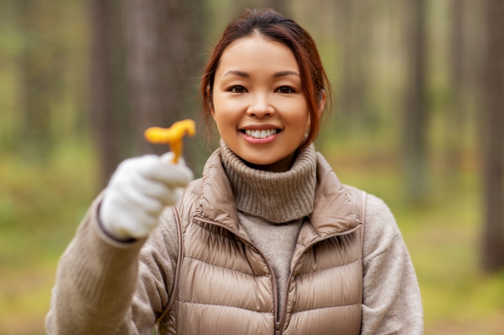 picking season, leisure and people concept - young asian woman with chanterelle mushroom in autumn forest. young woman picking mushrooms in autumn forest