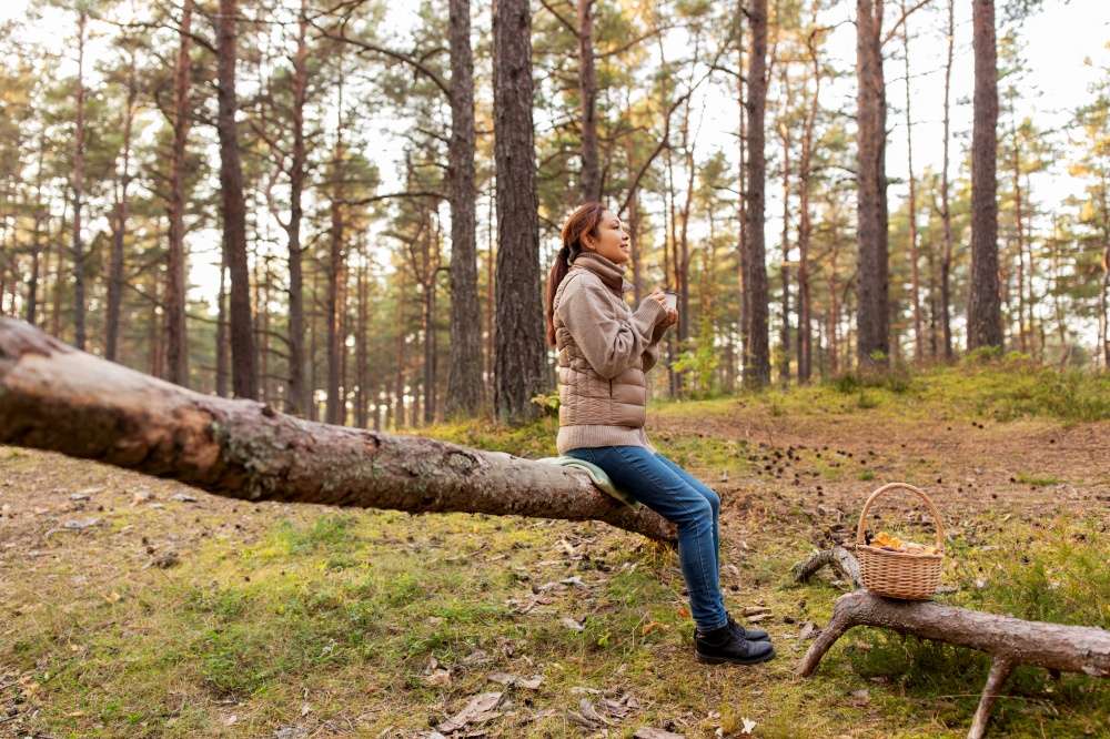 picking season, leisure and people concept - young asian woman with mushrooms in basket drinking tea in autumn forest. asian woman with mushrooms drinking tea in forest