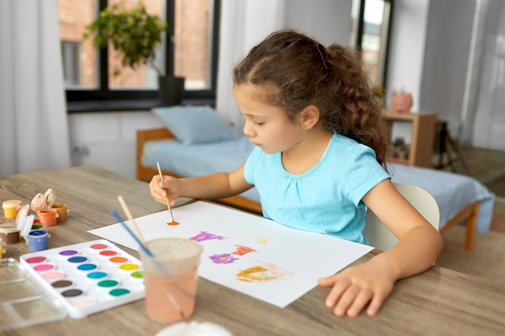 childhood, hobby and leisure concept - little girl drawing picture with colors and brush at home. little girl with colors drawing picture at home