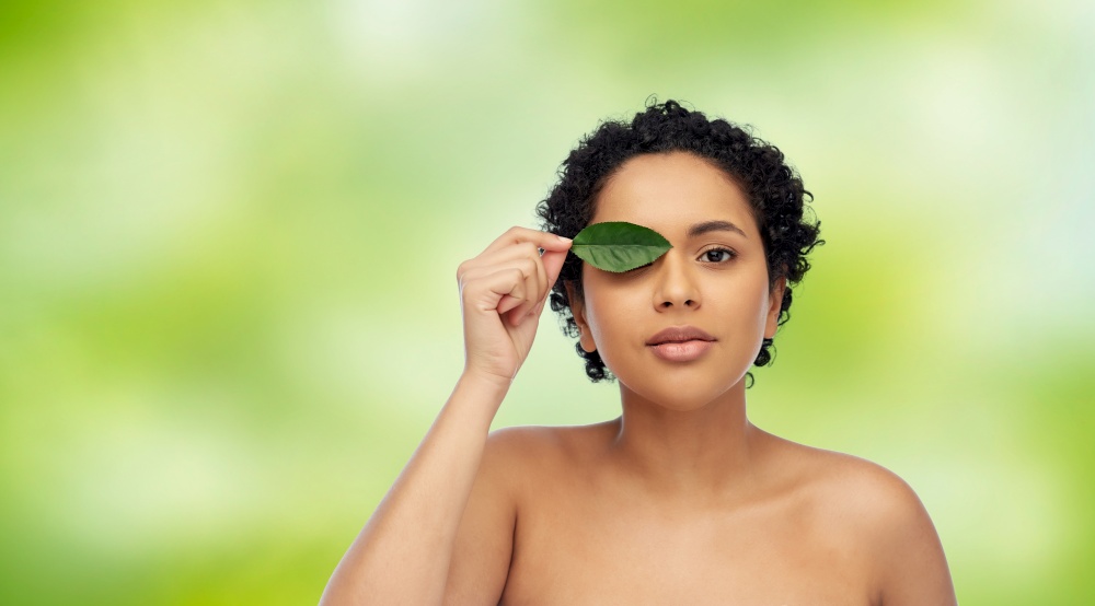 beauty, nature and people concept - portrait of young african american woman with green leaf over green natural background. portrait of african american woman with green leaf