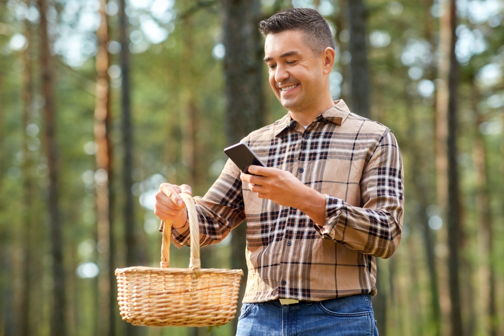 picking season, technology and leisure people concept - middle aged man with wicker basket and smartphone using app to identify mushroom in autumn forest. man using smartphone to identify mushroom
