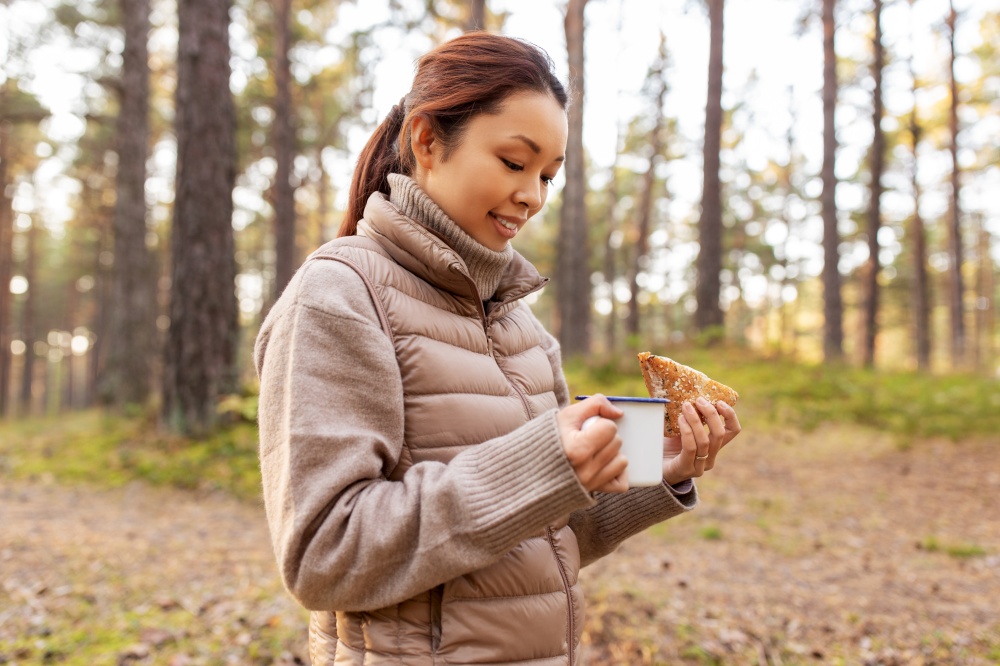 picking season, leisure and people concept - young asian woman with mushrooms in basket drinking tea and eating sandwich in autumn forest. woman with mushrooms drinks tea and eats in forest