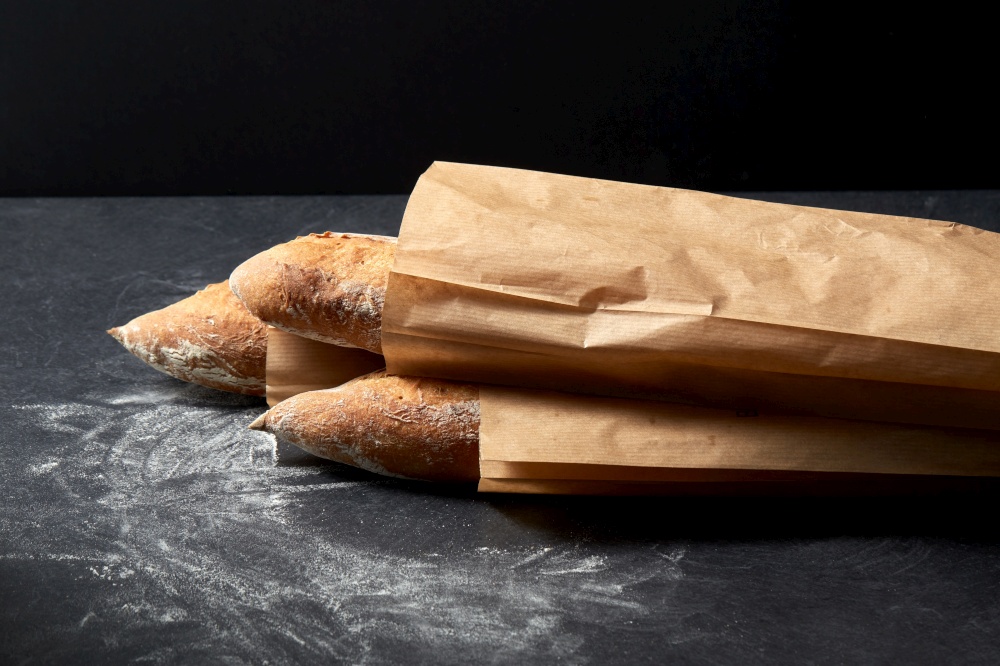food, baking and cooking concept - close up of baguette bread in paper bags on table over dark background. close up of baguette bread in paper bags on table