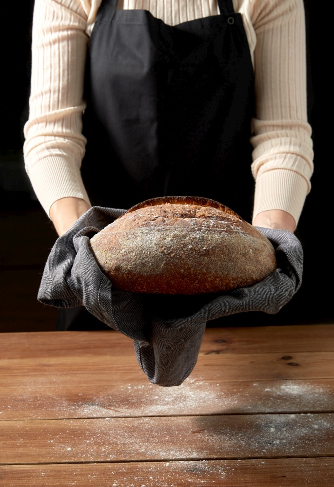 food cooking, baking and people concept - female baker with loaf of bread at bakery or kitchen. female baker with homemade bread at bakery