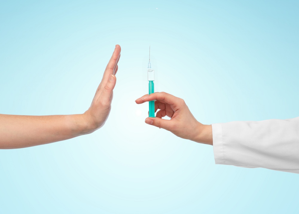 medicine, vaccination and healthcare concept - hand of doctor with syringe and patient showing stop gesture over blue background. hand with syringe and showing stop gesture