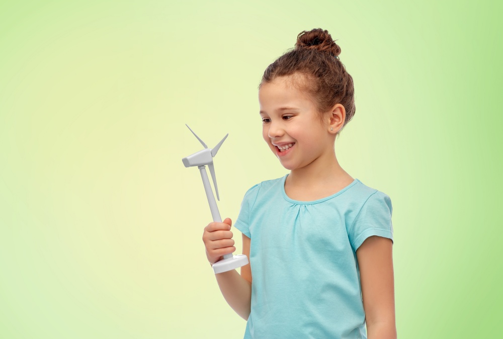 sustainable energy, power and people concept - happy smiling girl with toy wind turbine over green background. smiling girl with toy wind turbine
