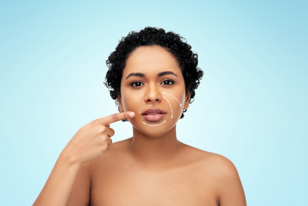beauty, plastic surgery and people concept - young african american woman with arrows on face over blue background. young african american woman with arrows on face