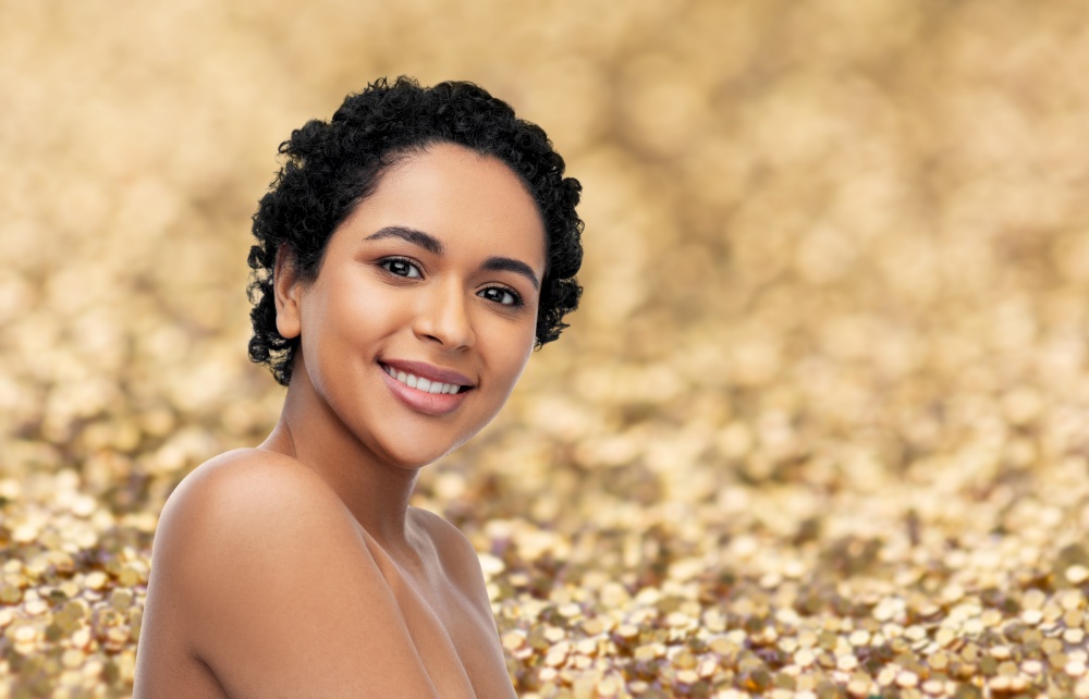beauty and people concept - portrait of happy smiling young african american woman with bare shoulders over golden glitter background. portrait of young african american woman