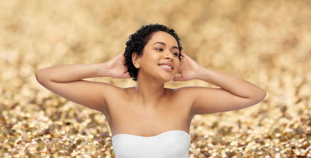 beauty and people concept - portrait of happy smiling young african american woman with bare shoulders touching her hair over golden glitter background. portrait of young african american woman