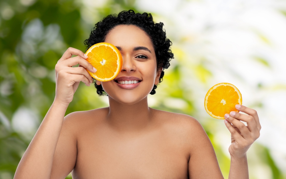 beauty, skin care and detox concept - smiling beautiful african american woman making eye mask of oranges over green natural background. smiling african woman making eye mask of oranges