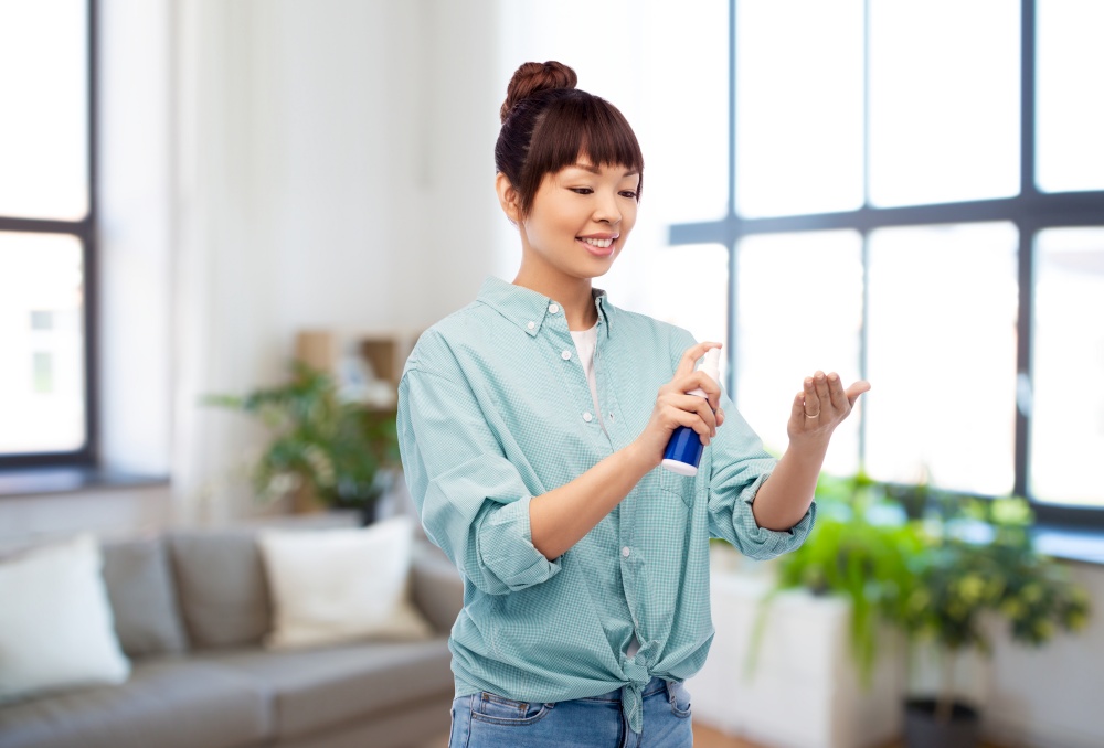 health care, safety and people concept - happy smiling asian woman using hand sanitizer over home living room background. happy smiling asian woman using hand sanitizer