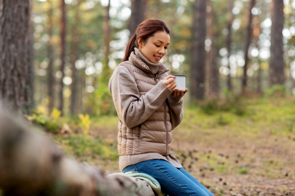 picking season, leisure and people concept - young asian woman with mug drinking tea in autumn forest. asian woman with mug drinking tea in forest