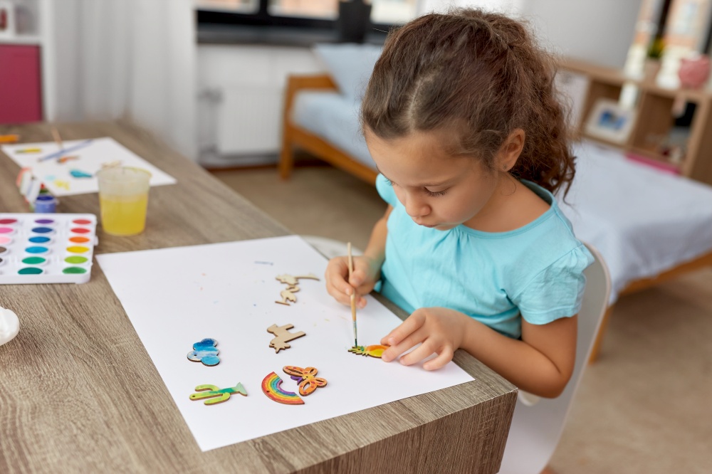 childhood, hobby and leisure concept - little girl with brush painting wooden chipboard items at home. little girl painting wooden items at home