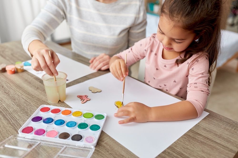 family, motherhood and leisure concept - mother spending time with her little daughter with colors painting chipboard items at home. mother with little daughter drawing at home