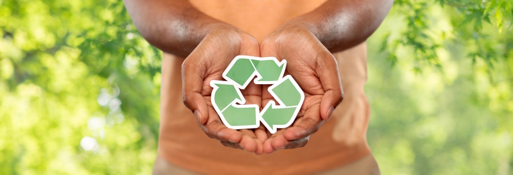 eco living, environment and sustainability concept - close up of young african american man in polo t-shirt holding green recycling sign over natural background. close up of man holding green recycling sign