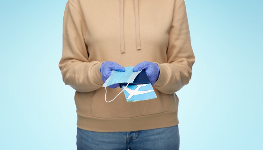 safe travel, tourism and health care concept - close up of woman in gloves with mask, passport and air ticket over blue background. woman with mask, passport and air ticket