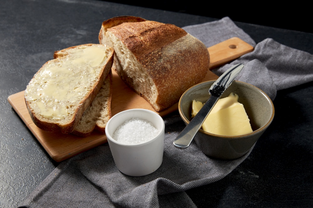 food, baking and cooking concept - close up of bread, butter in bowl, table knife and salt in cup on towel. close up of bread, butter, knife and salt on towel