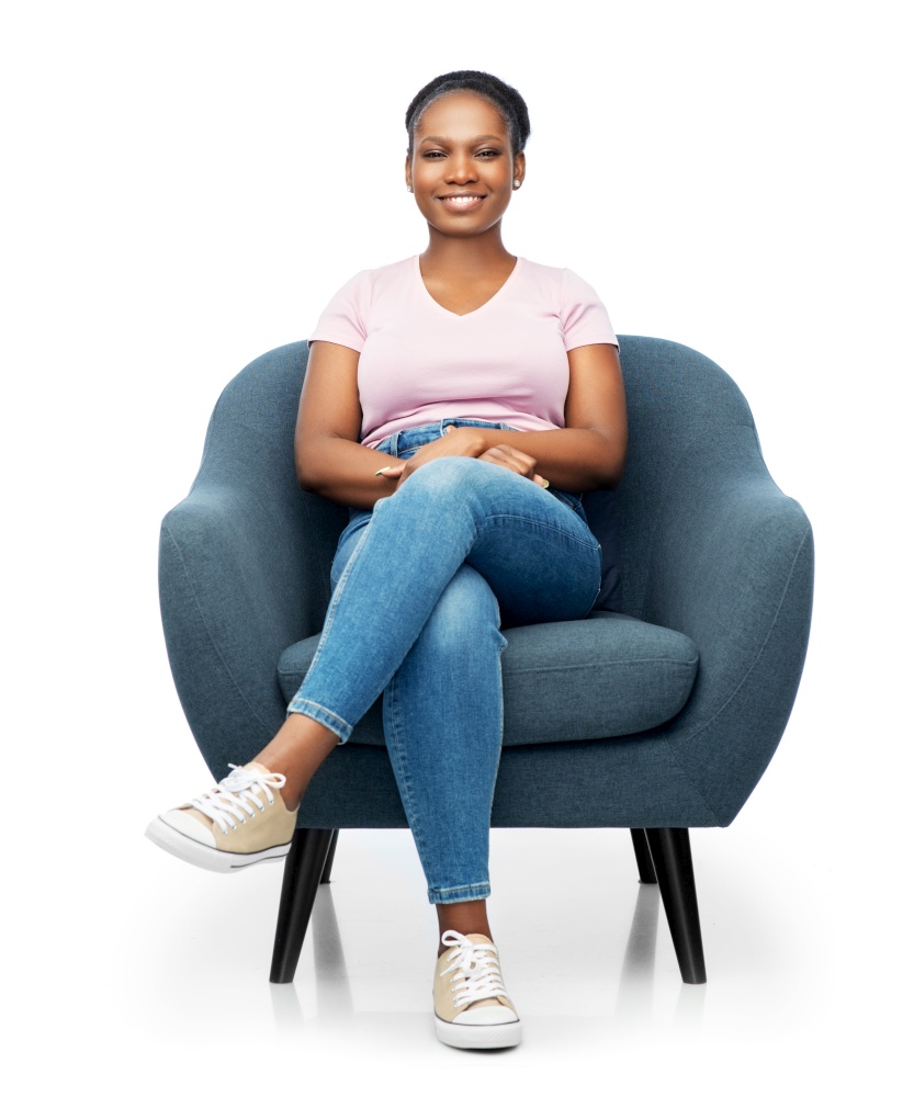 comfort, people and furniture concept - portrait of happy smiling young african american woman sitting in modern armchair over white background. smiling african american woman sitting in armchair