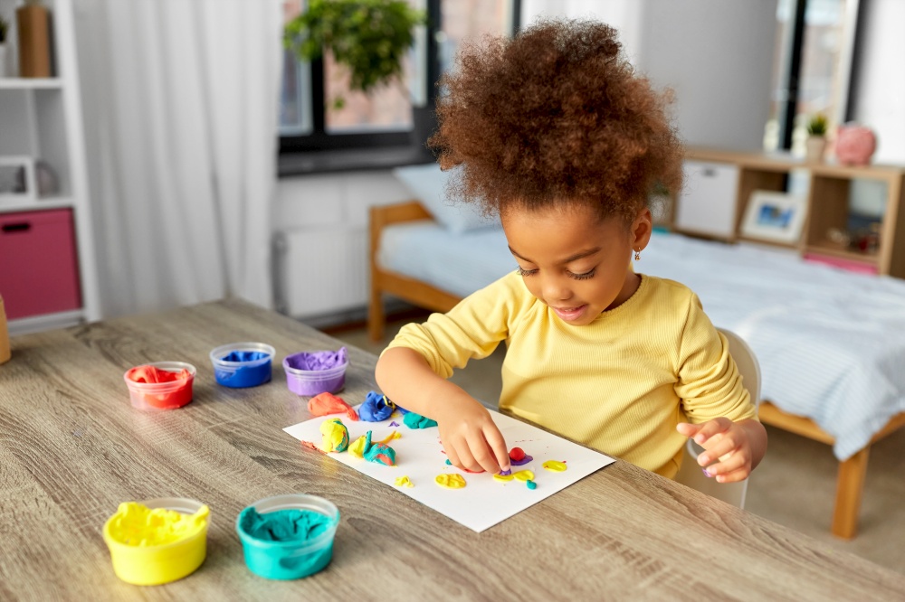 childhood, creativity and hobby concept - little african american girl with modeling clay playing at home. little girl with modeling clay playing at home