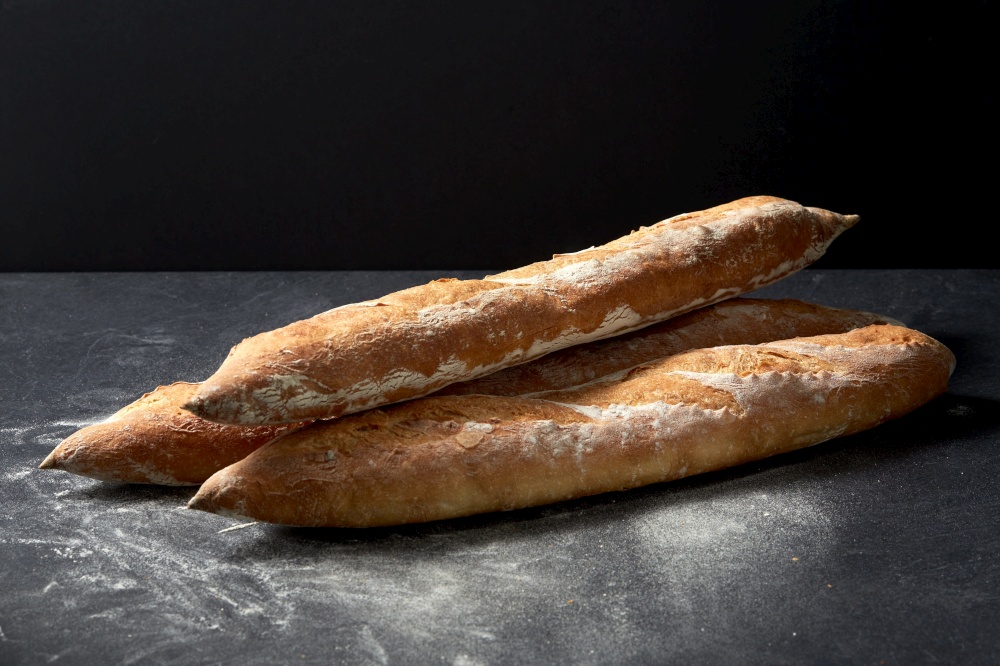 food, baking and cooking concept - pile of baguette bread on table over dark background. baguette bread on table over dark background