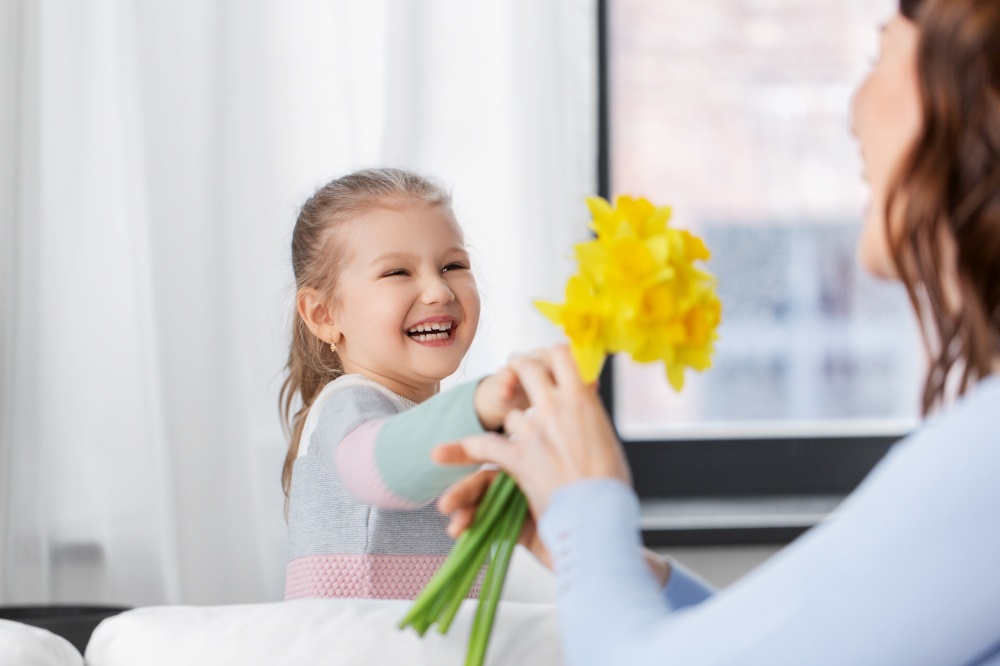 people, family and holidays concept - happy little daughter giving daffodil flowers to mother at home. happy daughter giving daffodil flowers to mother