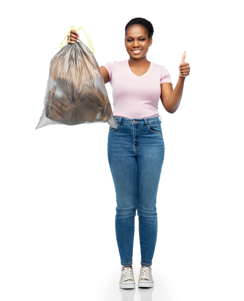 waste sorting and sustainability concept - smiling young african american woman holding plastic trash bag showing thumbs up over white background. smiling woman holding plastic trash bag with waste