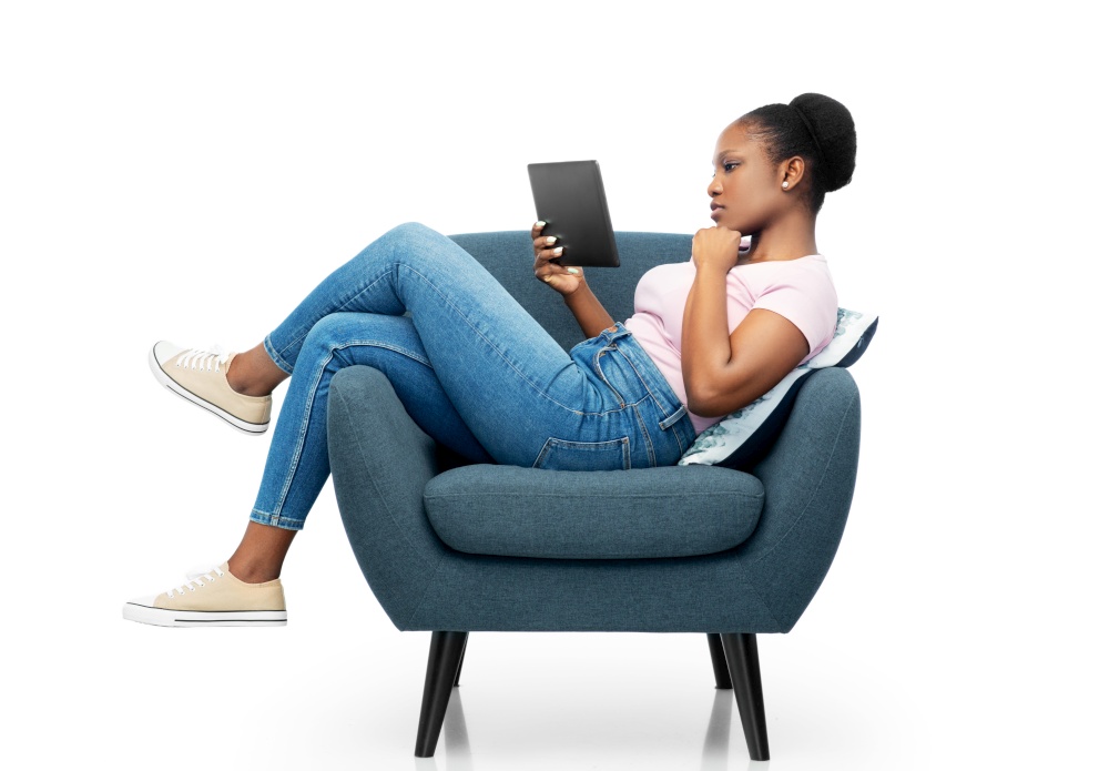 people and technology concept - young african american woman with tablet pc computer sitting in modern armchair over grey background. woman with tablet pc sitting in armchair