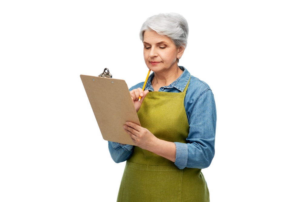 gardening, farming and old people concept - portrait of thinking senior woman in green garden apron with clipboard over white background. senior woman in garden apron with clipboard