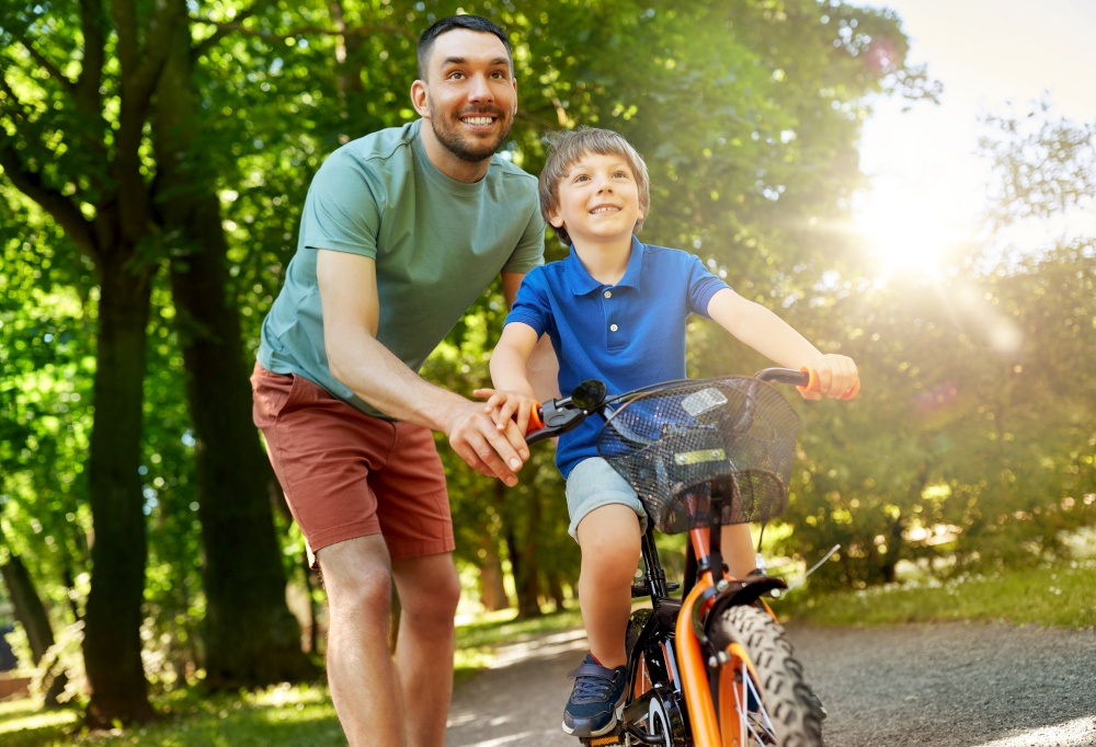 family, fatherhood and leisure concept - happy father teaching little son to ride bicycle at park. father teaching little son to ride bicycle at park