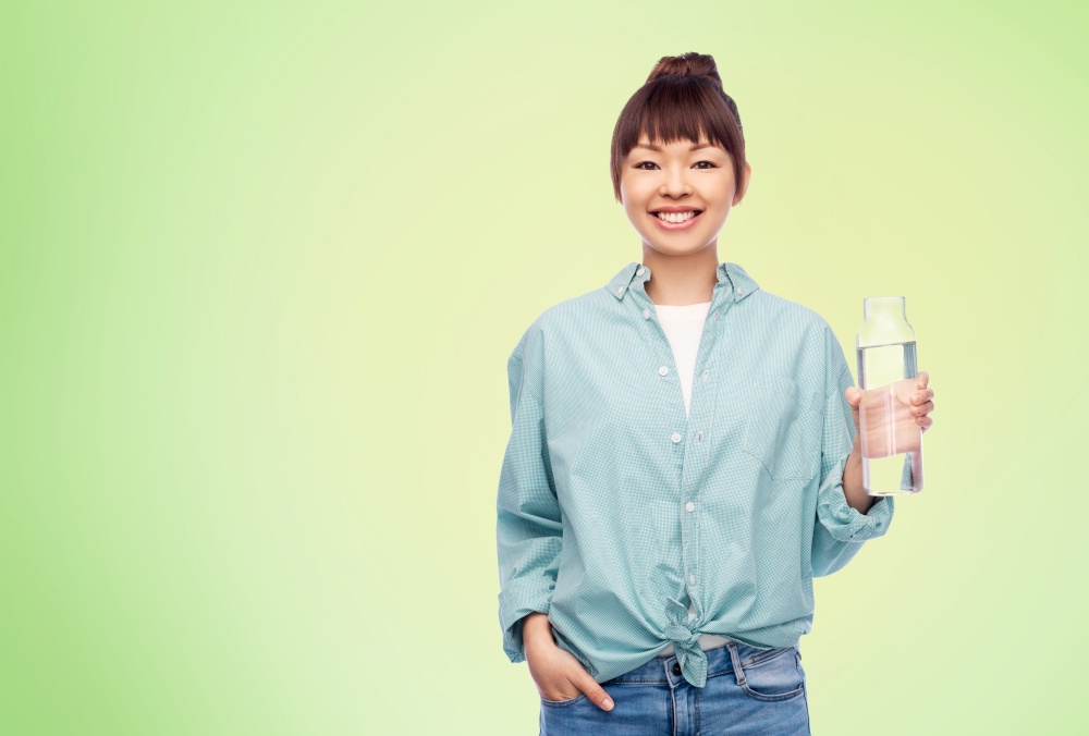 people concept - portrait of happy smiling young asian woman in turquoise shirt holding reusable glass bottle with water over lime green natural background. happy asian woman holding glass bottle with water