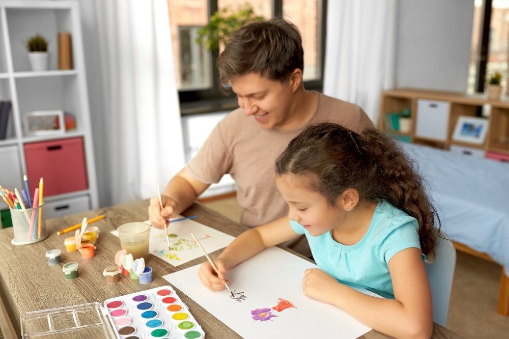 family, motherhood and leisure concept - happy smiling father spending time with his little daughter and drawing with colors at home. happy father with little daughter drawing at home