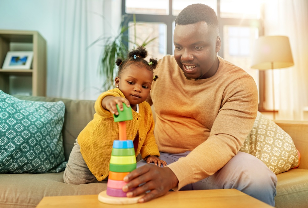 family, parenthood and people concept - happy african american father and baby daughter playing with toy blocks at home. african family playing with baby daughter at home
