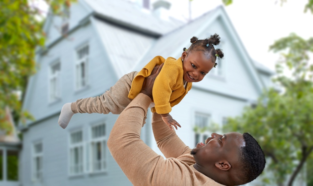 family, fatherhood and mortgage concept - happy african american father playing with baby daughter over house on background. happy african american father with baby daughter