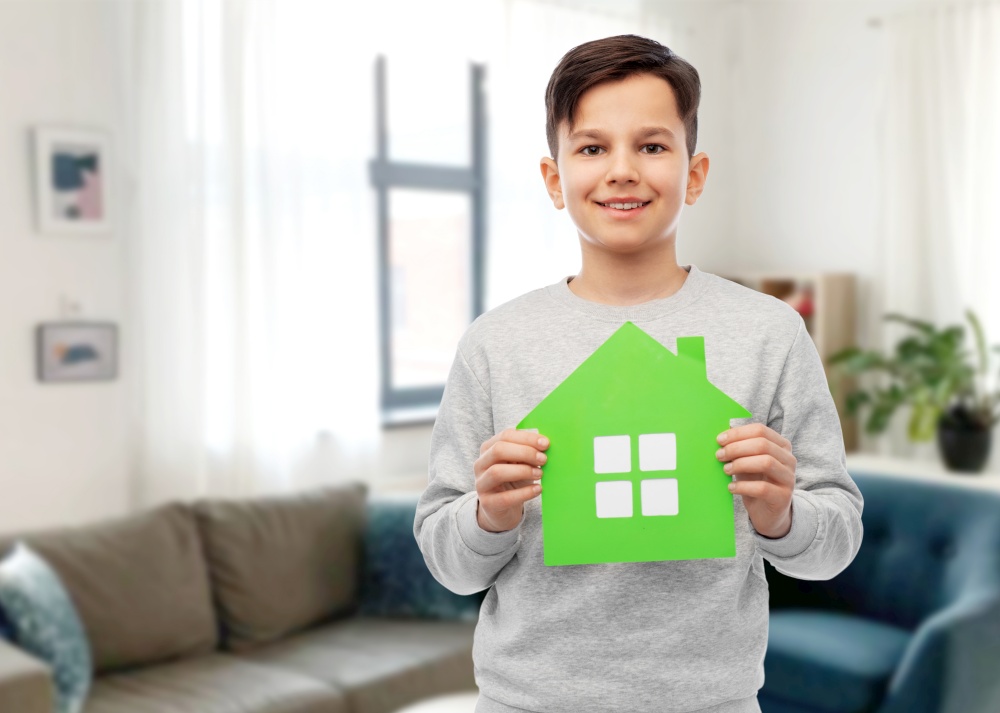 eco living, environment and sustainability concept - smiling boy holding green house icon over home room background. smiling boy holding green house icon