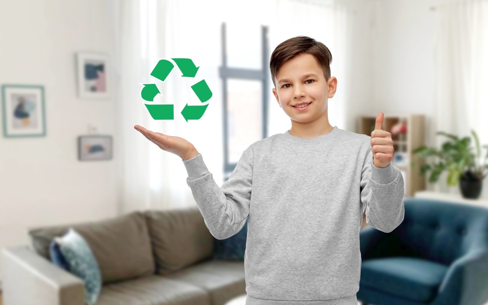 eco living, environment and sustainability concept - smiling boy holding green recycling sign and showing thumbs up over home room background. boy with green recycling sign showing thumbs up