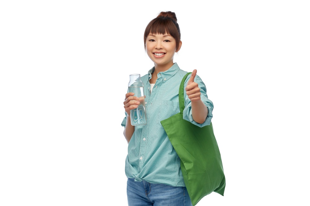 sustainability, eco living and people concept - portrait of happy smiling young asian woman with green reusable bag for food shopping and glass bottle of water showing thumbs up over white background. woman with bag for food shopping and glass bottle
