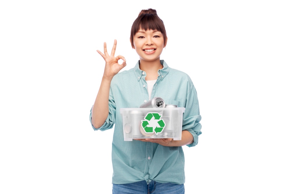 metal recycling, waste sorting and sustainability concept - smiling young asian woman holding plastic box with tin cans showing ok gesture over white background. smiling young asian woman sorting metallic waste