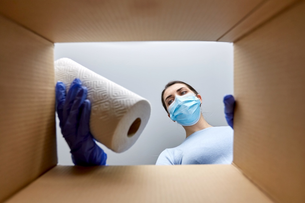 home delivery, shipping and pandemic concept - woman in protective medical mask and gloves opening parcel box, looking inside and taking cleaning supplies out. woman in mask taking cleaning supplies from box