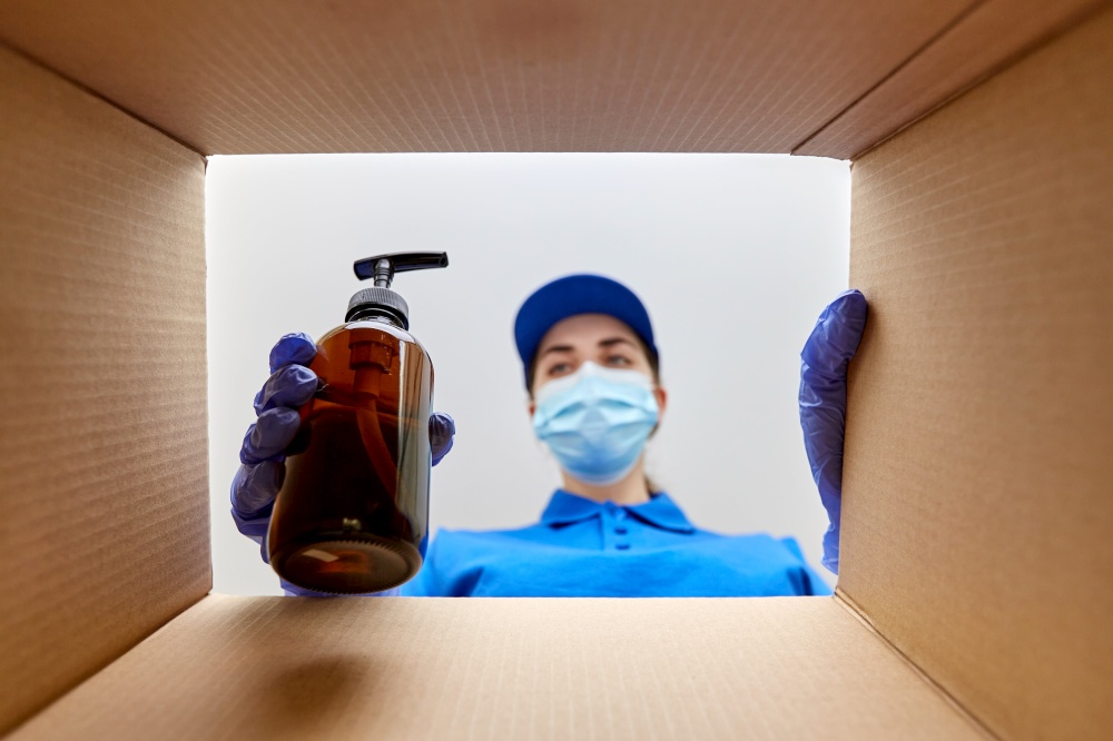 home delivery, shipping and pandemic concept - woman in protective medical mask and gloves packing parcel box with cosmetics and beauty products. woman in mask packing parcel box with cosmetics
