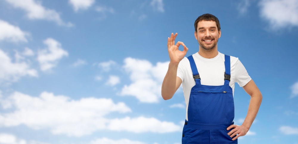 profession, construction and building concept - happy smiling male worker or builder showing ok hand sign over blue sky and clouds on background. happy smiling male worker or builder showing ok