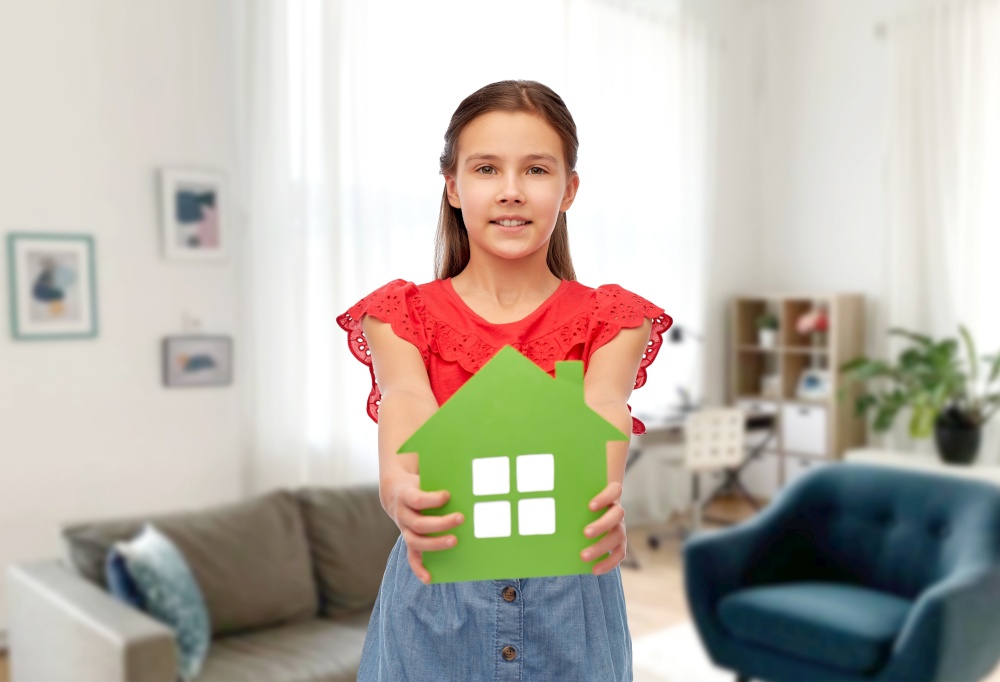 eco living, environment and sustainability concept - smiling little girl holding green house icon over home room background. smiling little girl holding green house icon