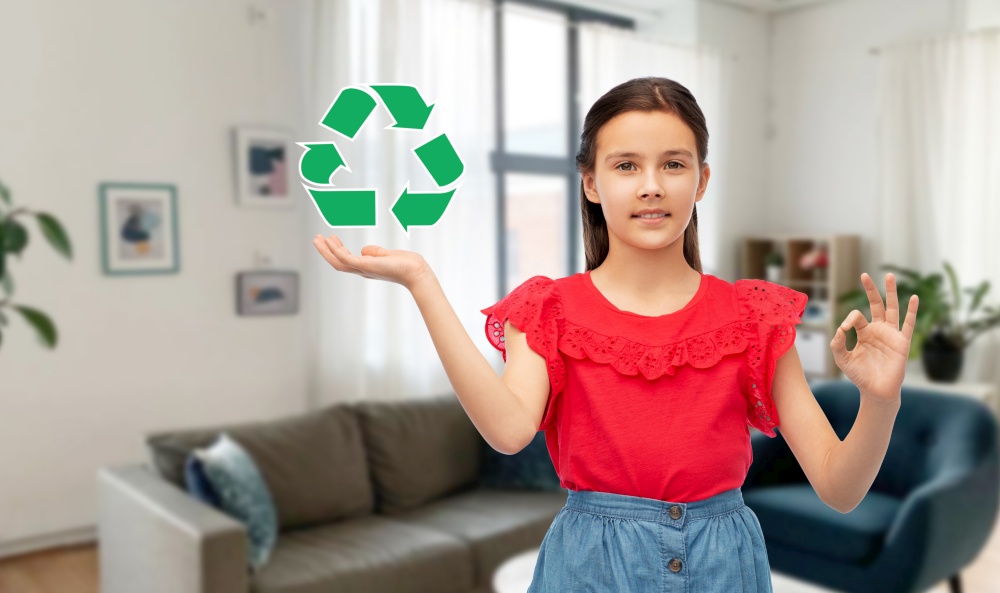 eco living, environment and sustainability concept - smiling girl holding green recycling sign showing ok gesture over home room background. smiling girl with green recycling sign showing ok