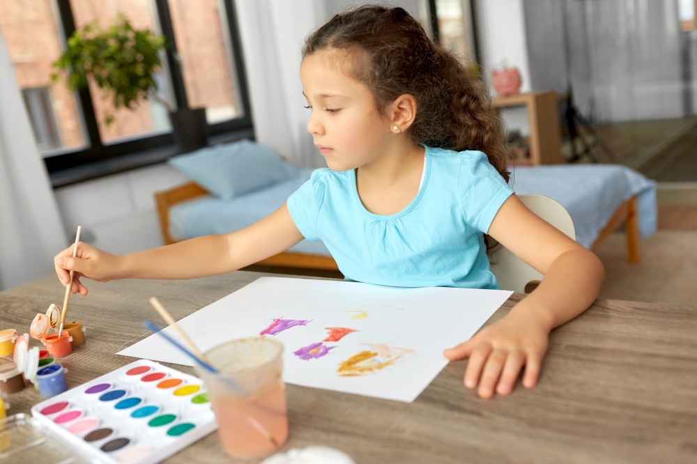 childhood, hobby and leisure concept - little girl drawing picture with colors and brush at home. little girl with colors drawing picture at home