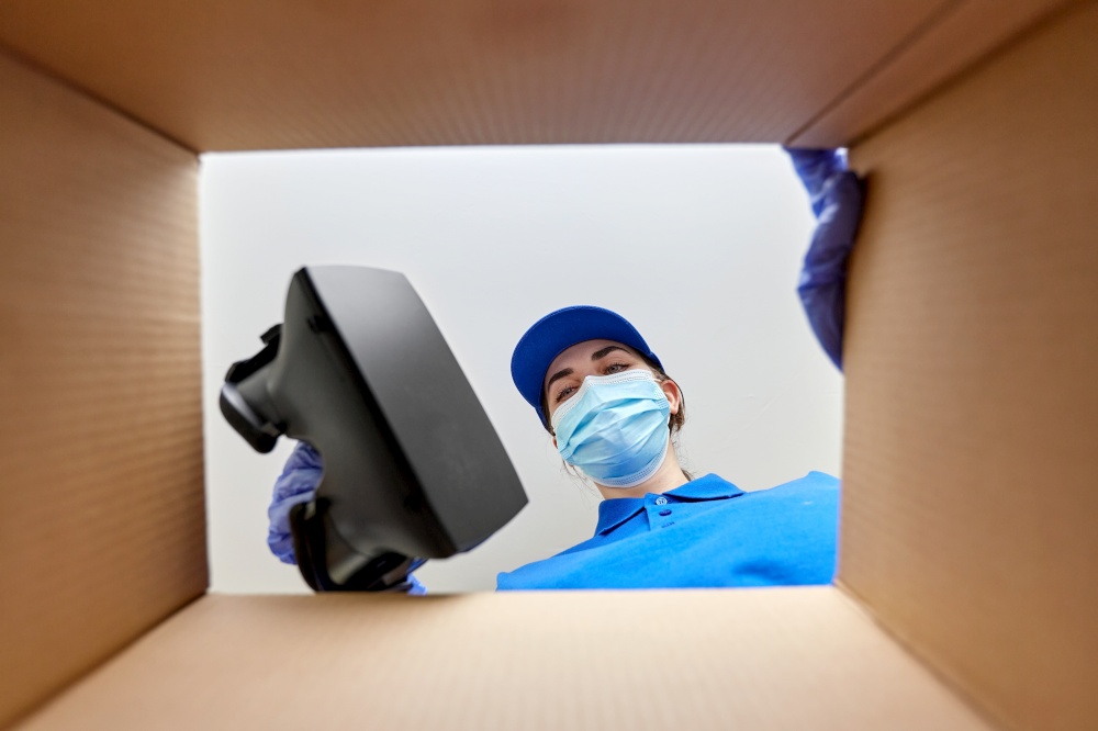 delivery, shipping and pandemic concept - woman in protective medical mask and gloves packing vr glasses to parcel box. woman in mask packing vr glasses to parcel box